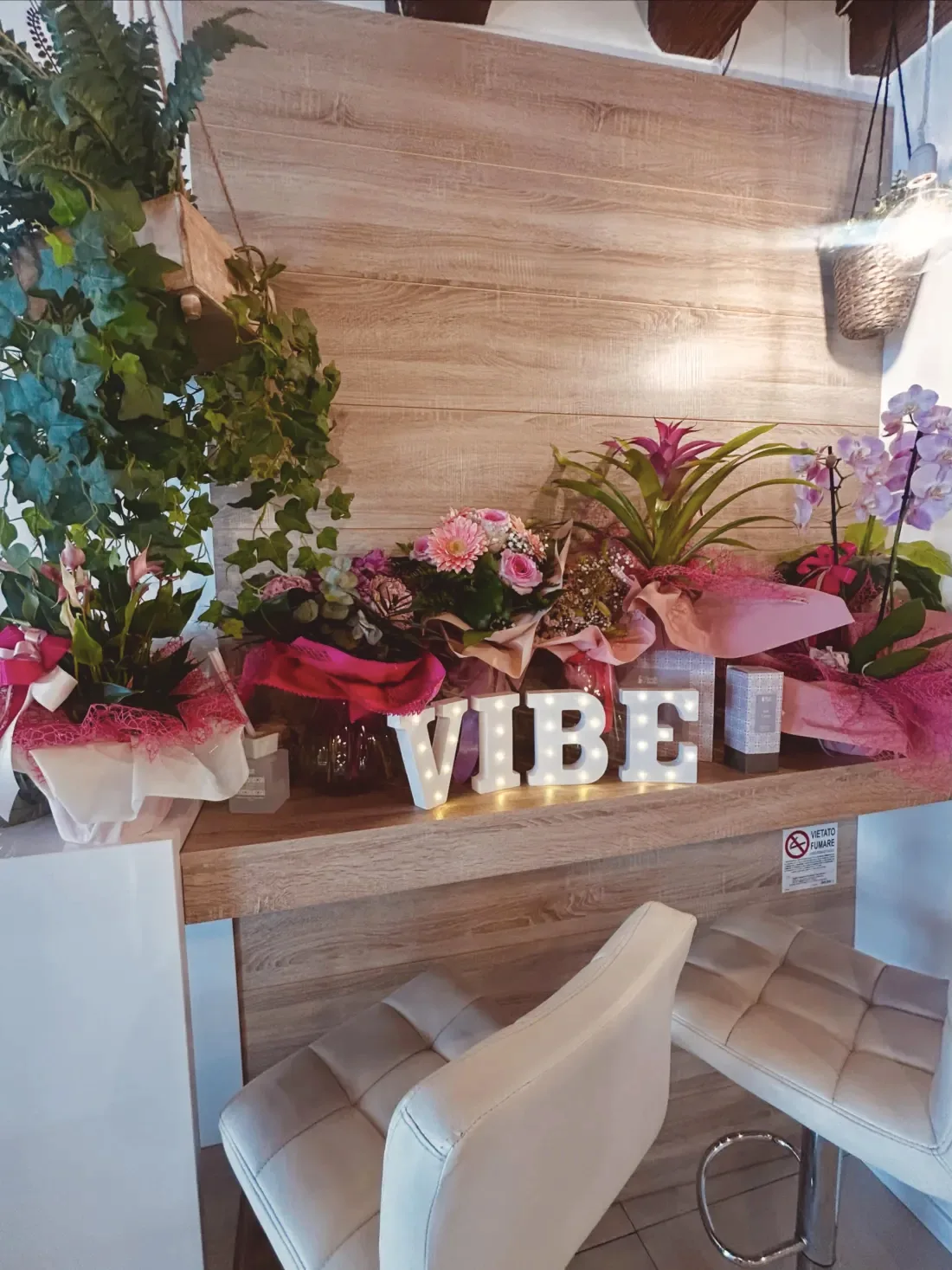 Interno di ViBe con le lettere luminose VIBE e composizioni floreali